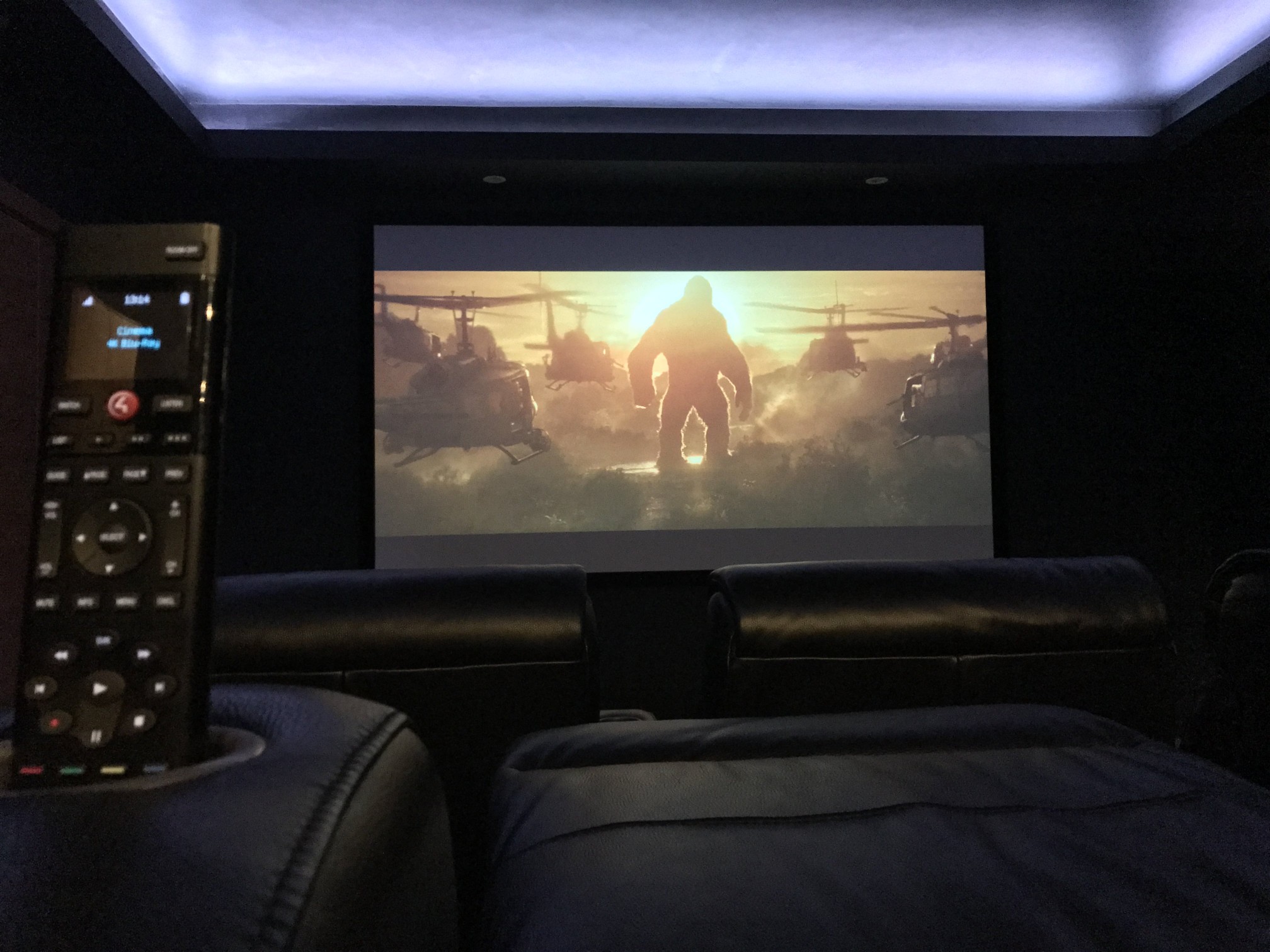 Home Cinema room with film on projector screen, lighting, cinema chairs, and Control4 remote